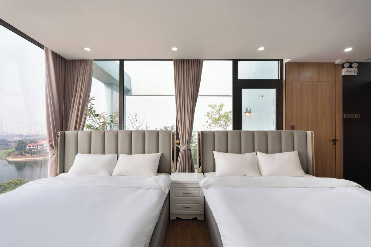 Une chambre d’hôtel moderne avec deux lits, une vue sur un plan d’eau et un paysage urbain.