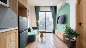 Una sala de estar moderna con un sofá, una mesa redonda, una planta en maceta, un televisor de pantalla plana y un amplio ventanal con cortinas.