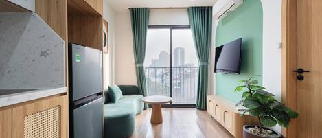 Una sala de estar moderna con un sofá, una mesa redonda, una planta en maceta, un televisor de pantalla plana y un amplio ventanal con cortinas.