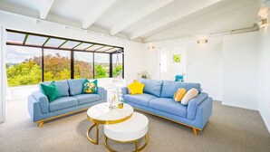 A modern living room with two blue sofas, a white coffee table, and a large window with a view of trees. - Enjoy Your Private SPA with Stunning Tranquil View (Auckland)