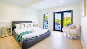 A bedroom with a bed, bedside tables, a chair, and a view through a sliding door. - Enjoy Your Private SPA with Stunning Tranquil View (Auckland)