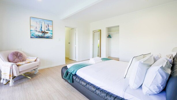 A modern bedroom with a large bed, a chair, a painting, and a wardrobe. - Enjoy Your Private SPA with Stunning Tranquil View (Auckland)
