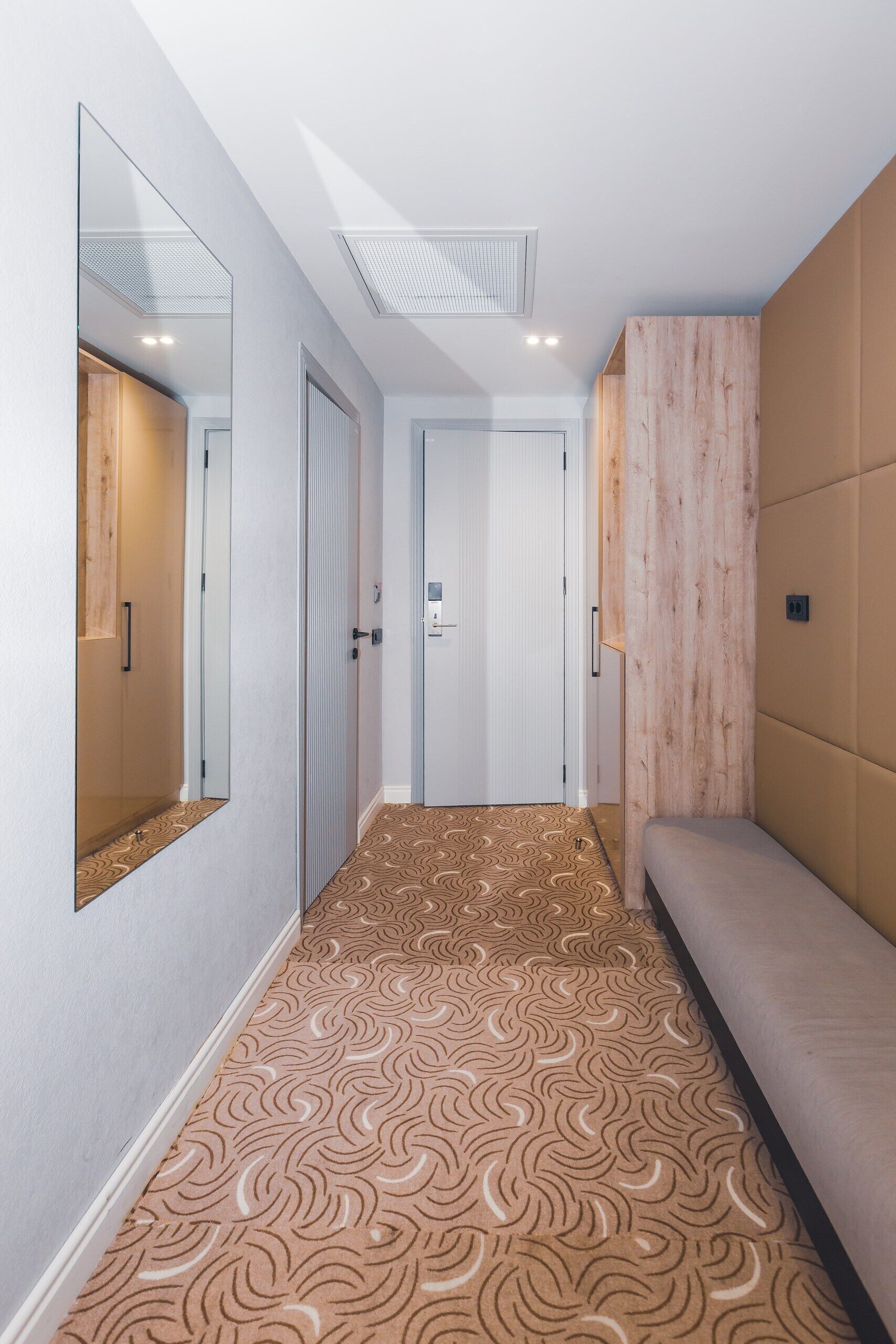 A hallway with patterned carpet, a bench, and mirrored walls.