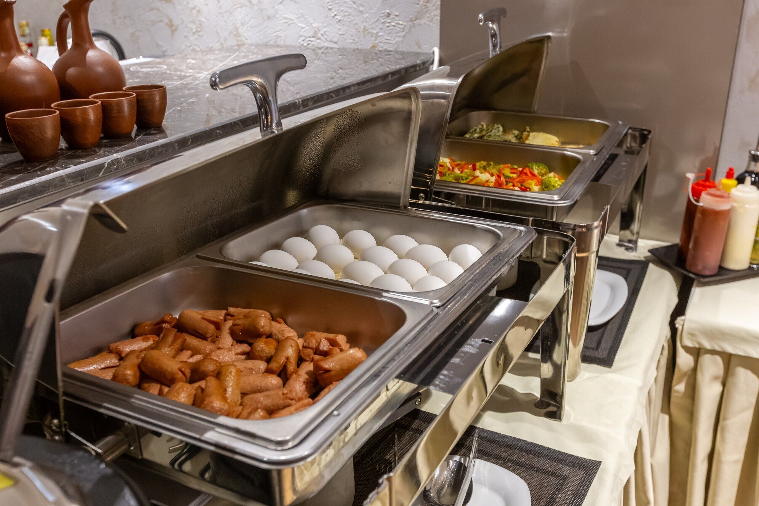 A buffet setup with various food items including eggs, sausages, and vegetables.