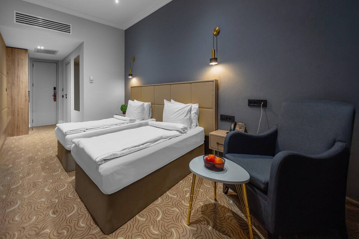 Ein Hotelzimmer mit einem großen Bett, einem Nachttisch mit Lampe, einem Sessel und einem kleinen Tisch mit Obst.