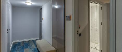 A hallway with a bench, a door with a number sign, and a patterned carpet.