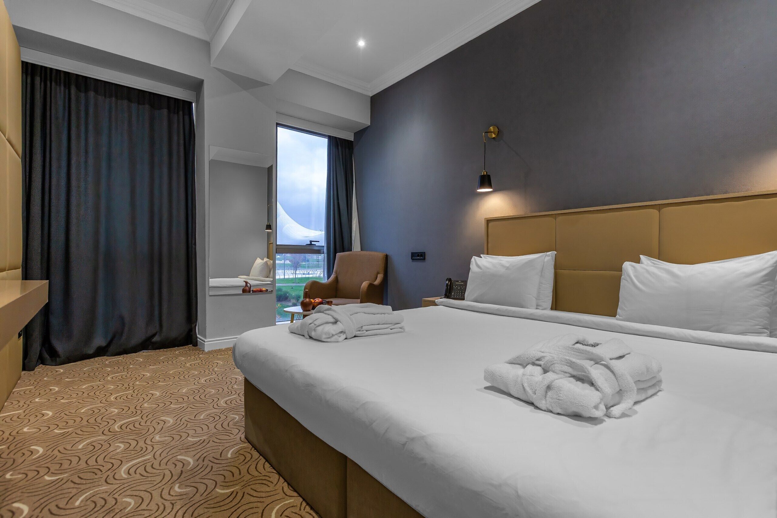 Camera d'albergo con un letto grande, una sedia, una scrivania e vista sull'esterno.