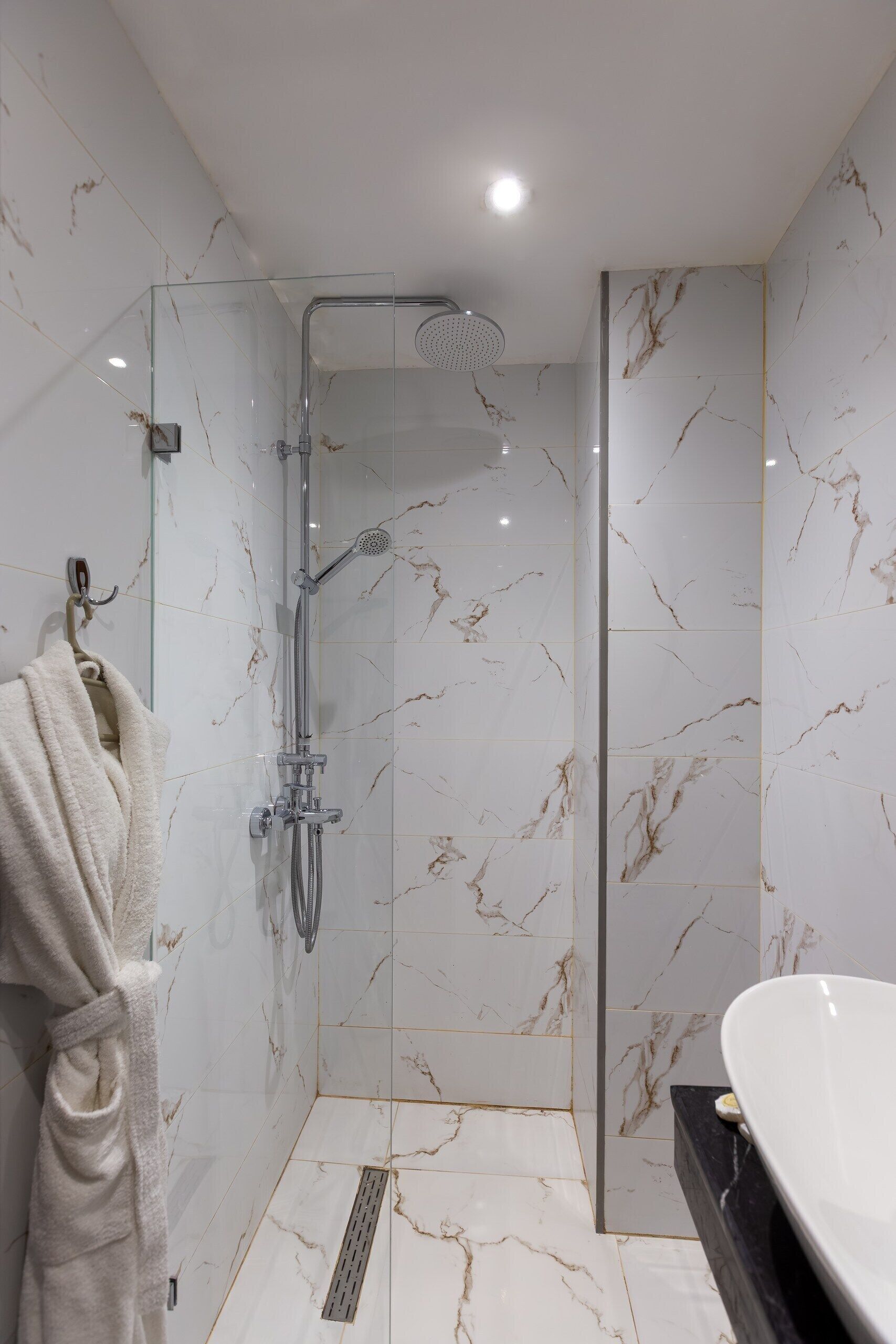A modern bathroom with a glass-enclosed shower, a white marble floor, and a black countertop with a white sink.