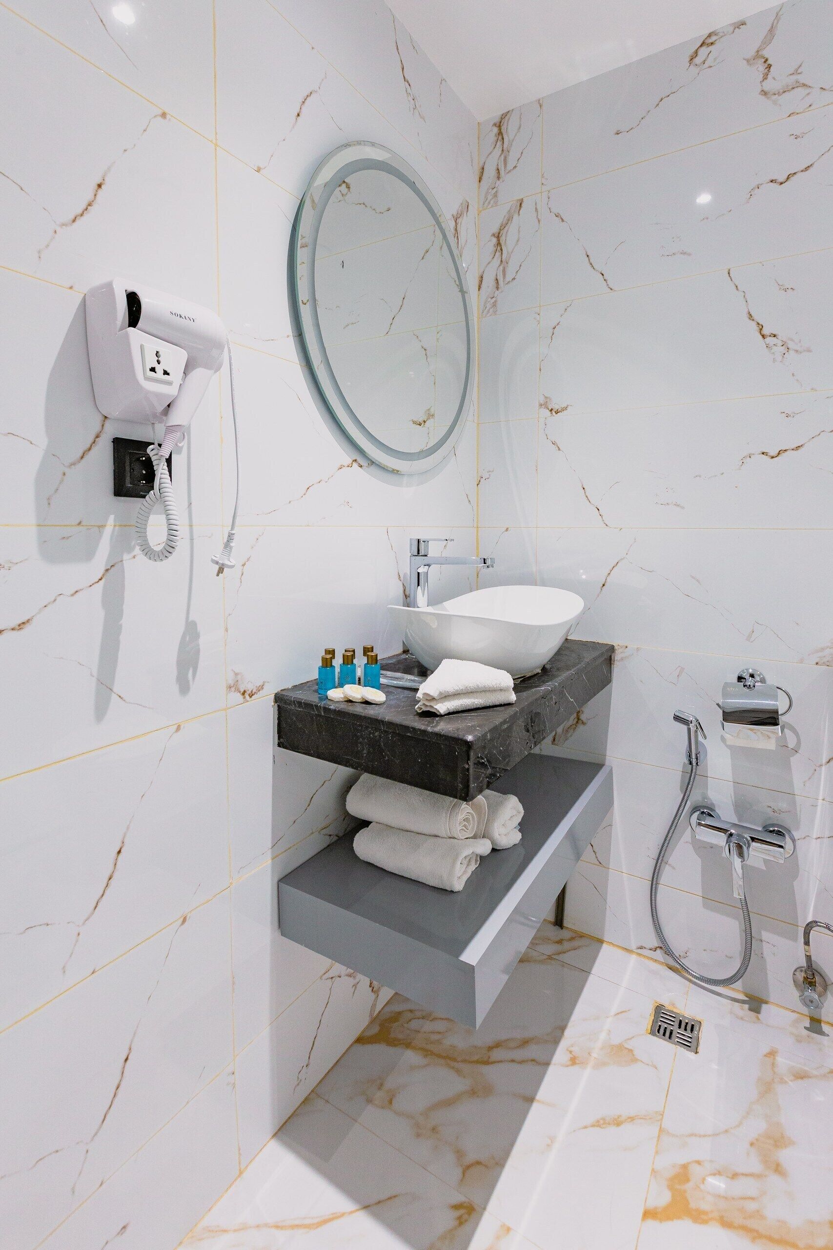 A modern bathroom with a marble floor, a white sink, a mirror, and a hairdryer on the wall.