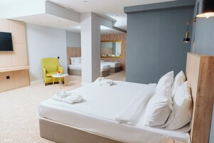 Hotelkamer met een groot bed, een stoel, een tafeltje en een aan de muur bevestigde televisie.