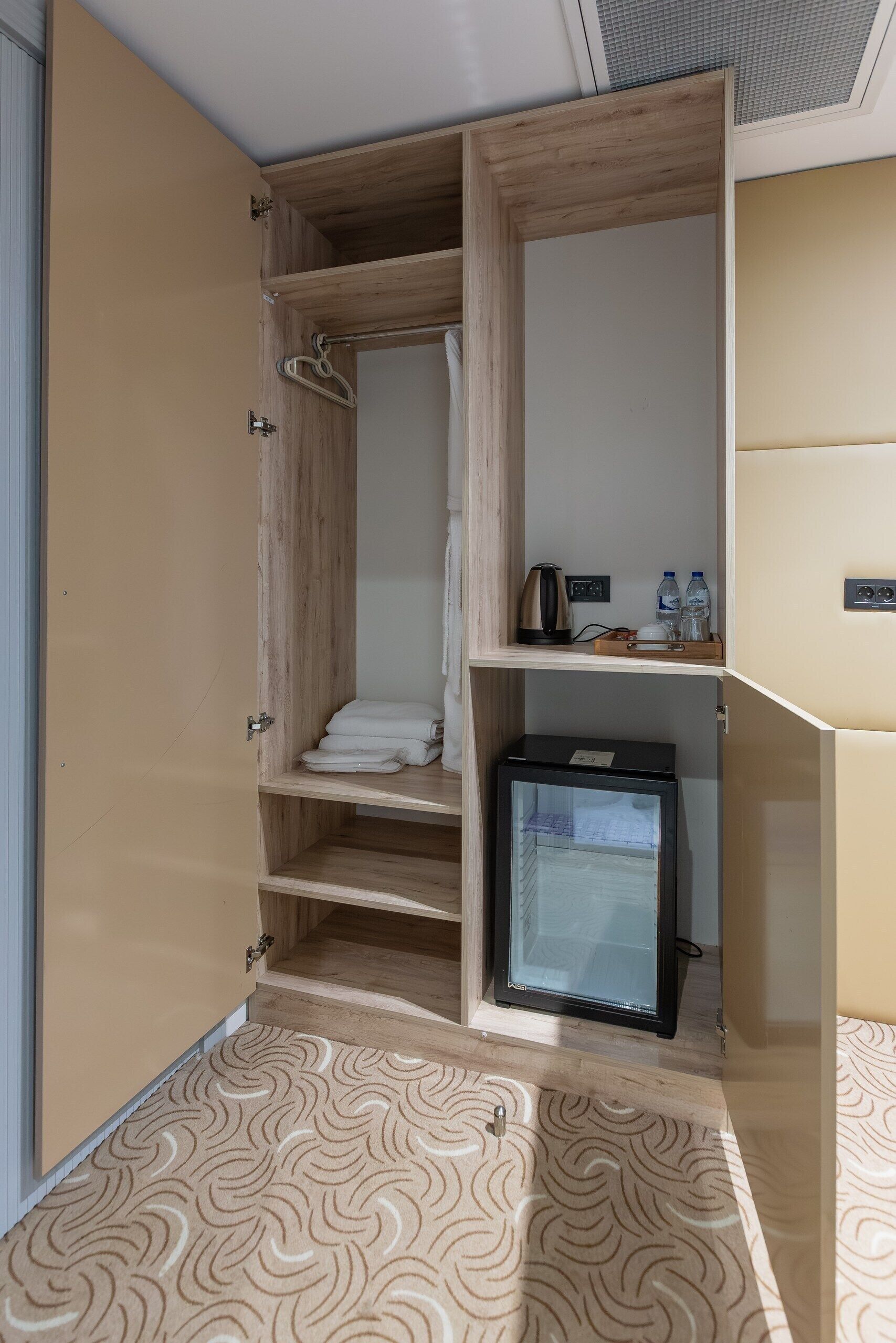 A compact room with a wooden wardrobe, a small refrigerator, and a patterned carpet.