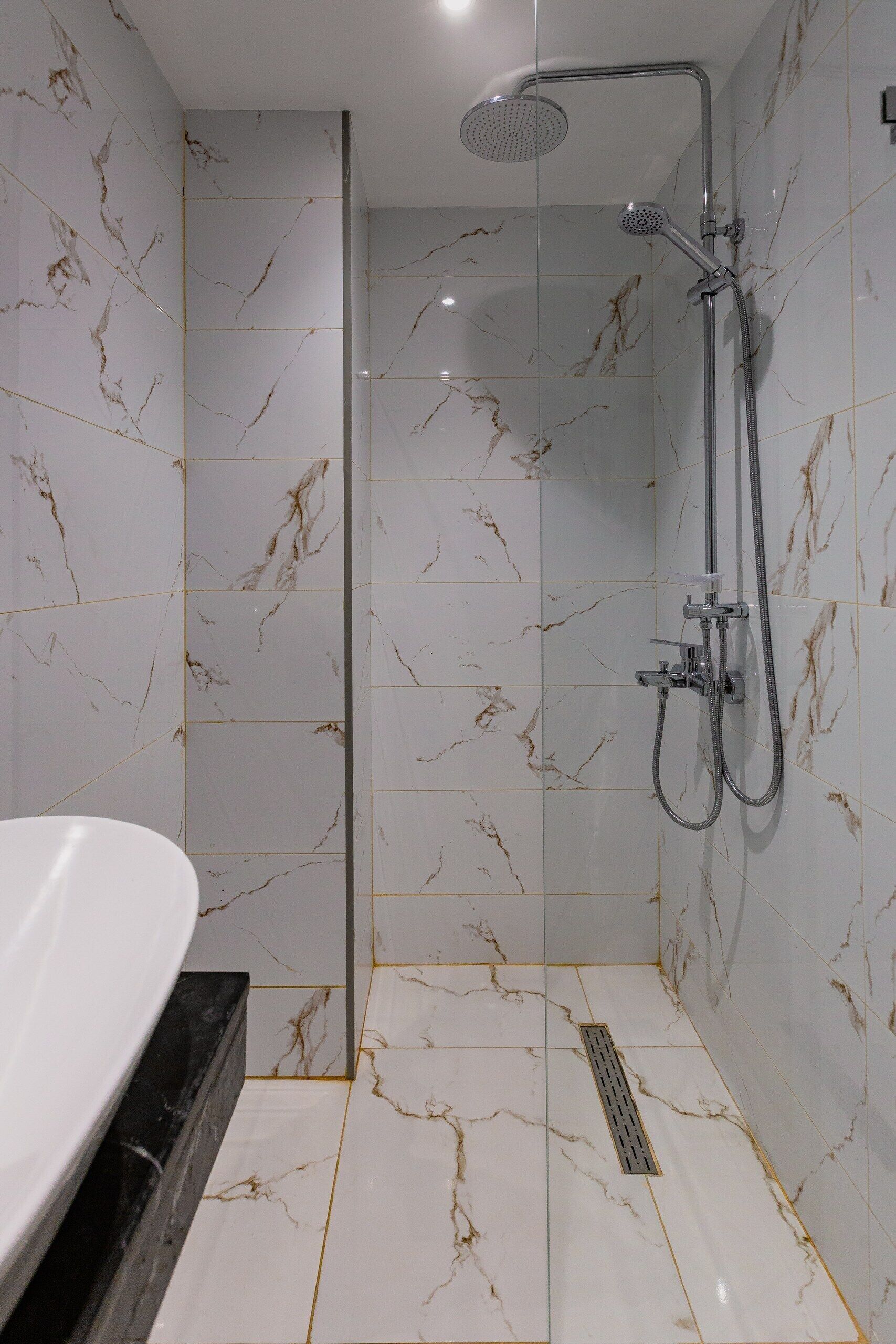 A modern bathroom with a glass-enclosed shower, marble tiles, and a white sink.