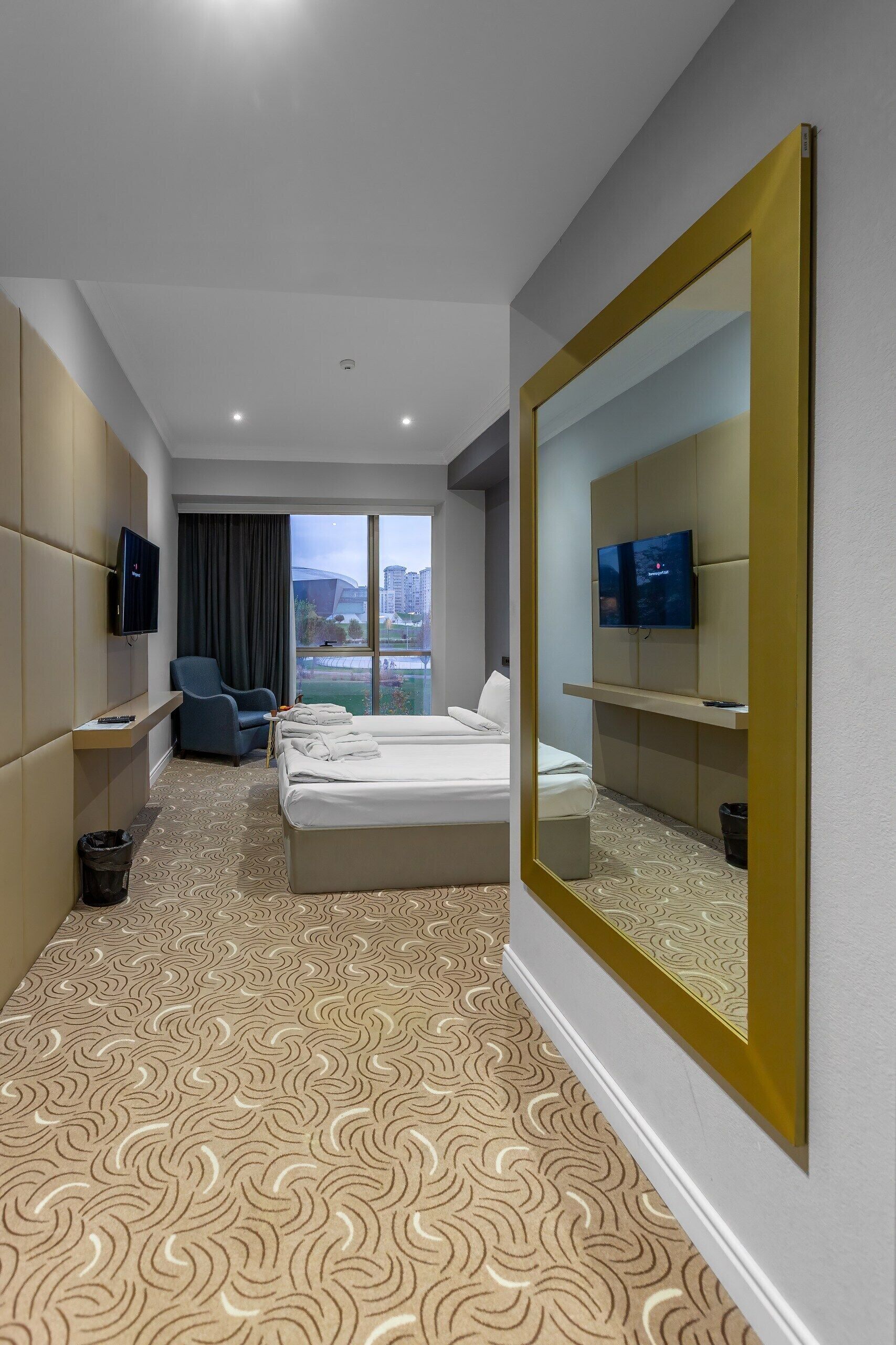 A hotel room with a bed, a chair, a TV, and a large mirror.