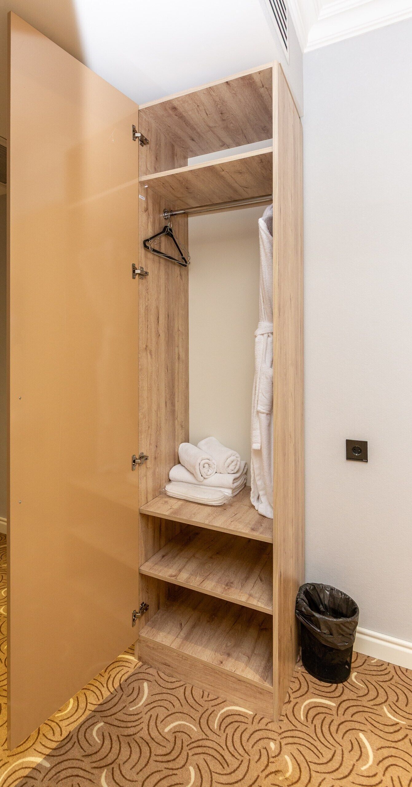 A wooden wardrobe with shelves, a hanging rack, and a small shelf with folded towels.