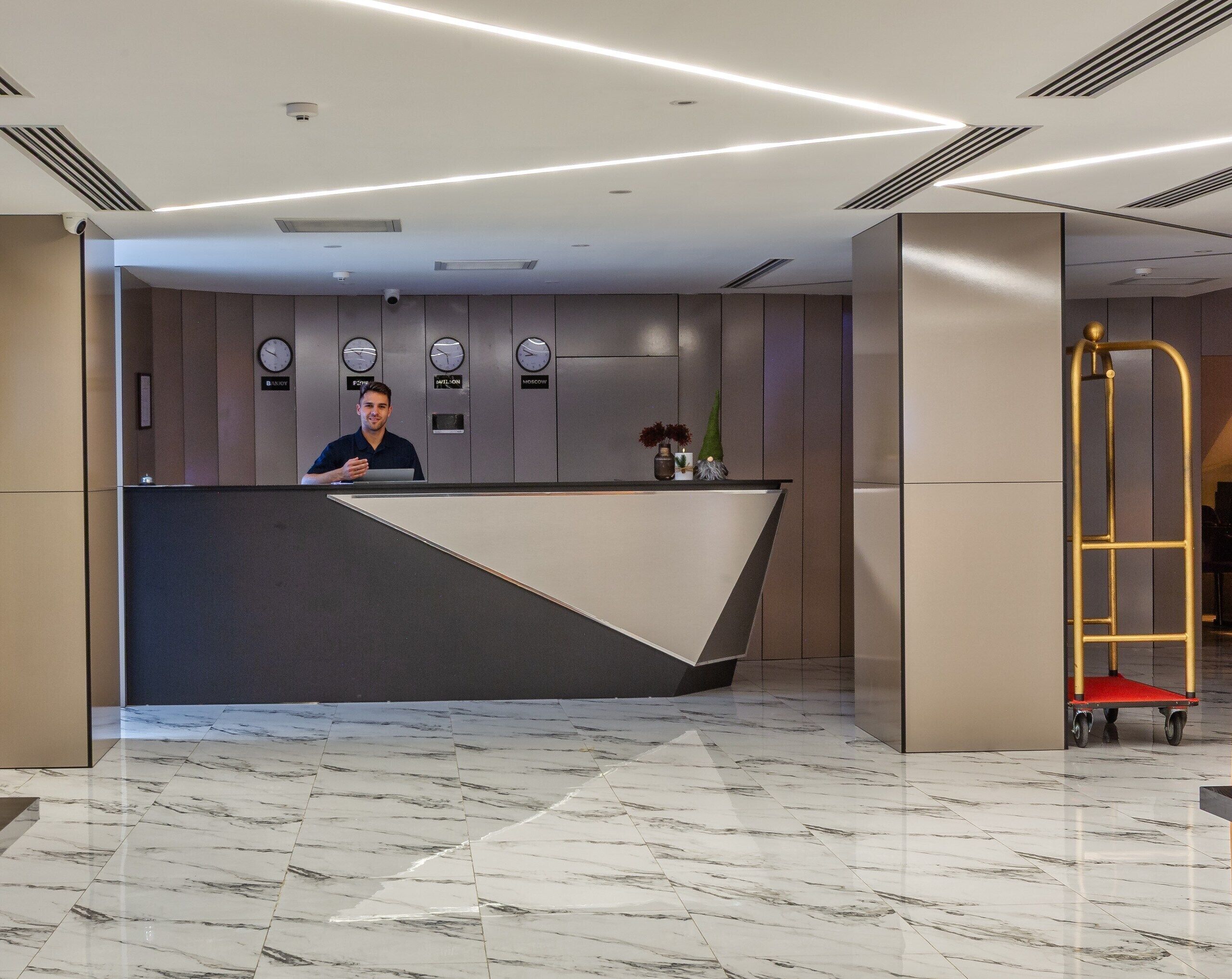 A modern reception desk with a digital clock, a security camera, and a small plant.