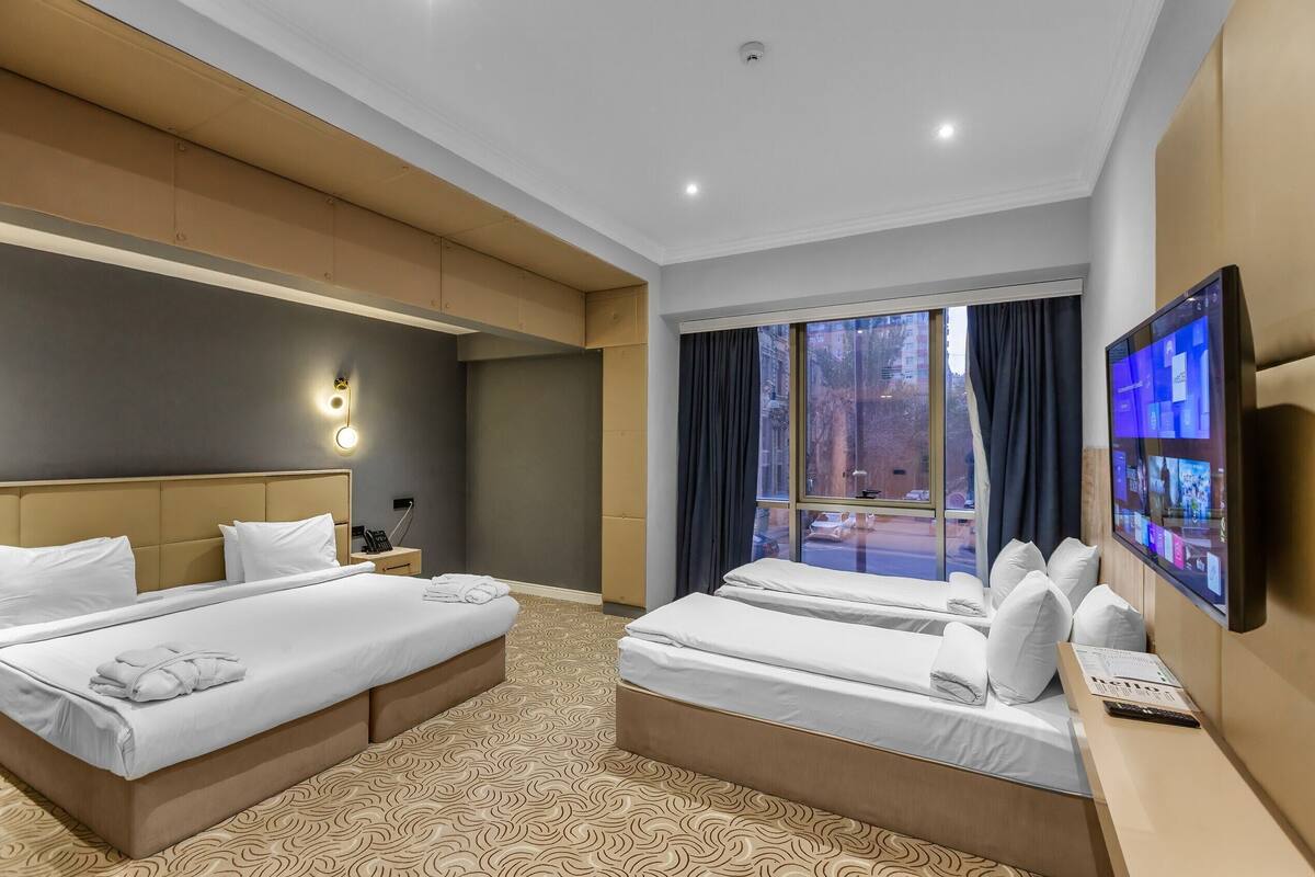 Ein Hotelzimmer mit zwei Betten, einem Fernseher, einem Schreibtisch und einem Fenster mit Vorhängen.