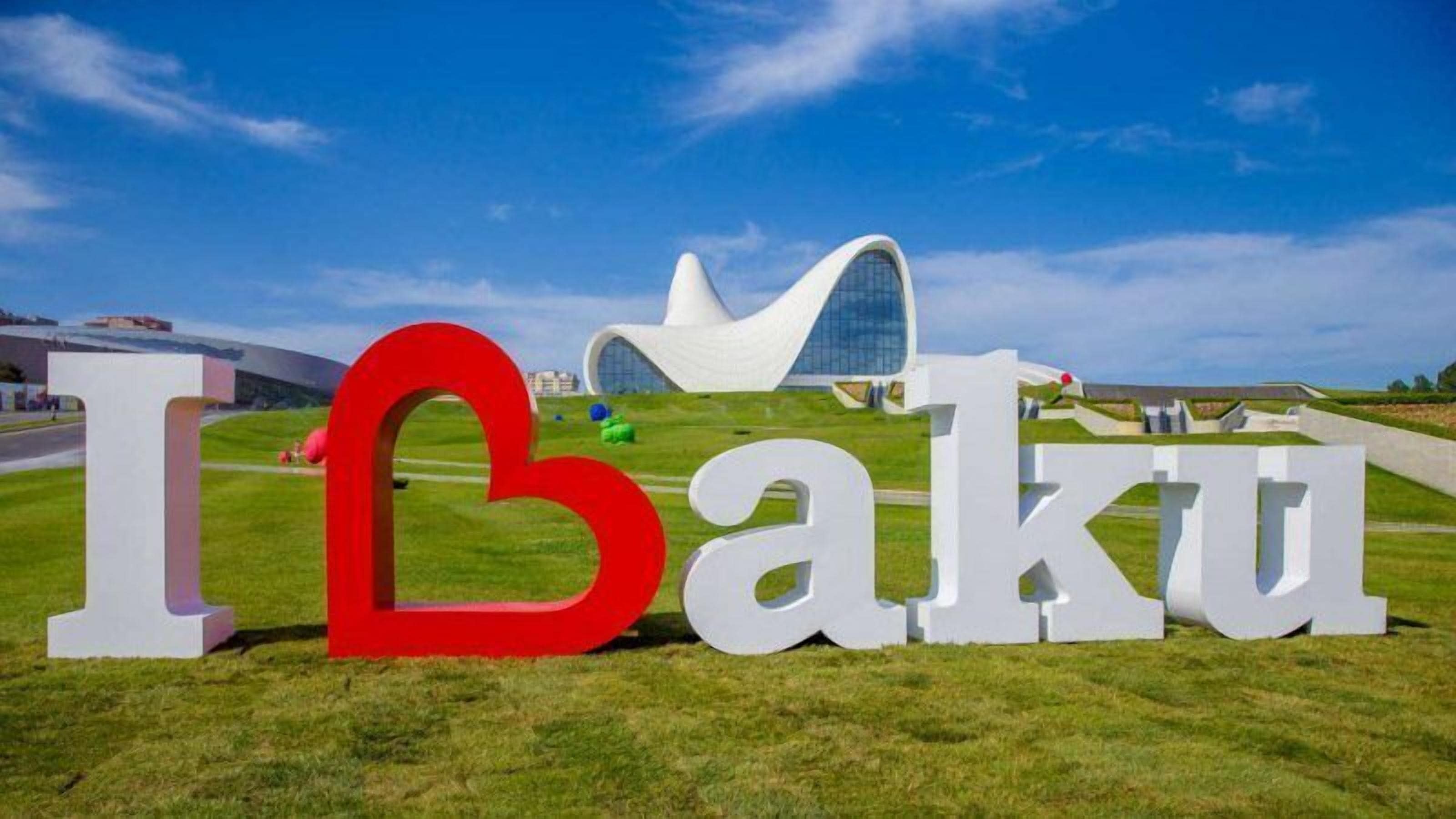 A large sign with the text "I Baku" in white and red letters, with a modern building in the background.