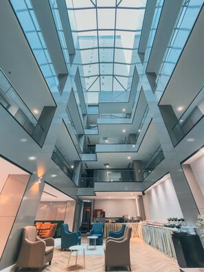 Ein modernes Interieur mit Glasdecke, mehreren Ebenen und einem Essbereich mit Tischen und Stühlen.