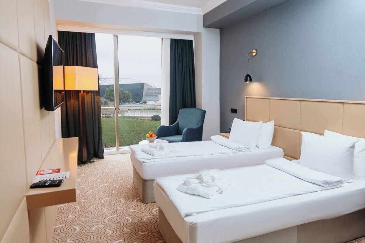 Ein Hotelzimmer mit zwei Betten, einem Fernseher, einem Sessel und Blick ins Freie.