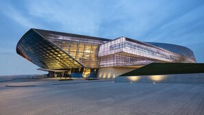 Een modern architecturaal gebouw met een uniek, golvend ontwerp, voorzien van grote glaspanelen en een ruim plein ervoor.
