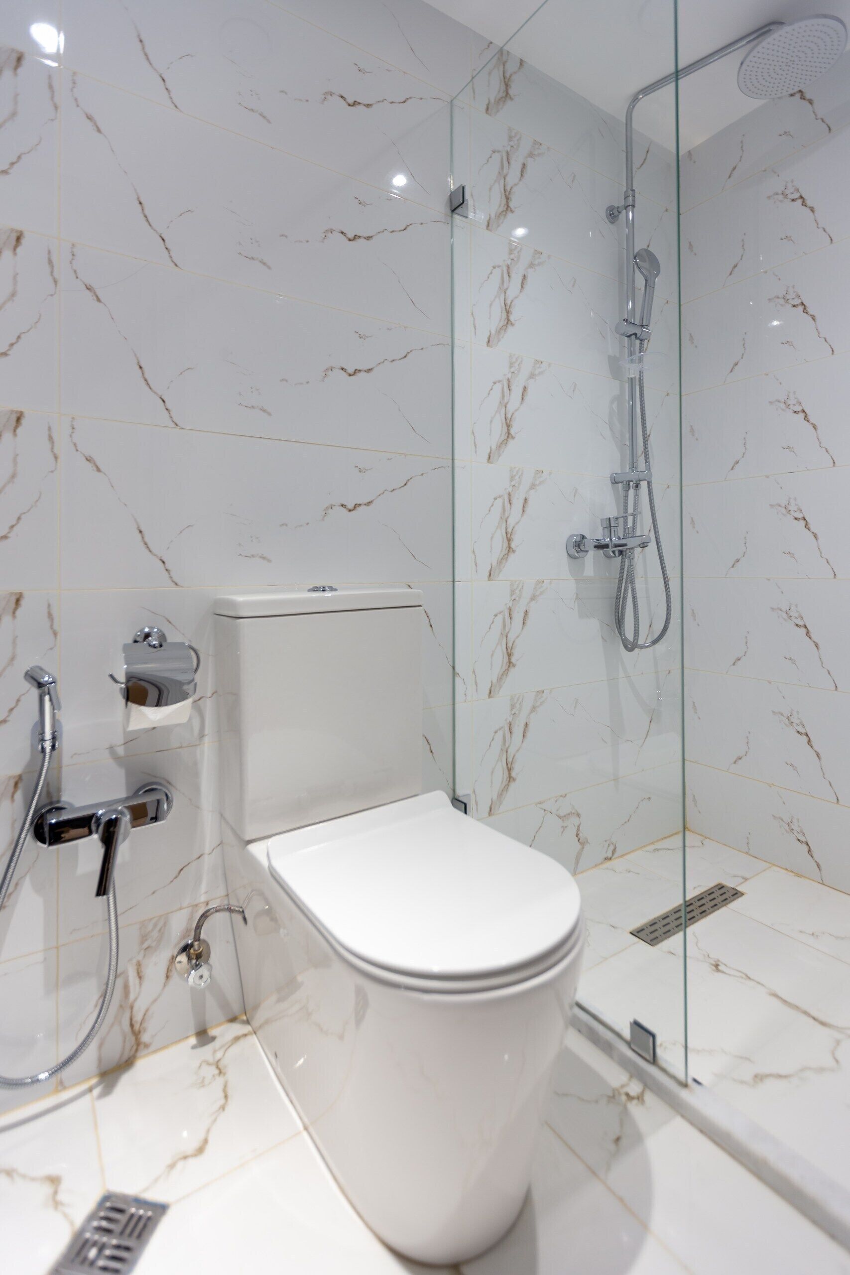 Une salle de bain moderne avec une douche à parois de verre, des toilettes et un mur recouvert de carreaux de marbre.