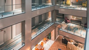Een meerlaags atrium met glazen balustrades, een centraal zitgedeelte met tafels en stoelen, en een keuken op de bovenverdieping.