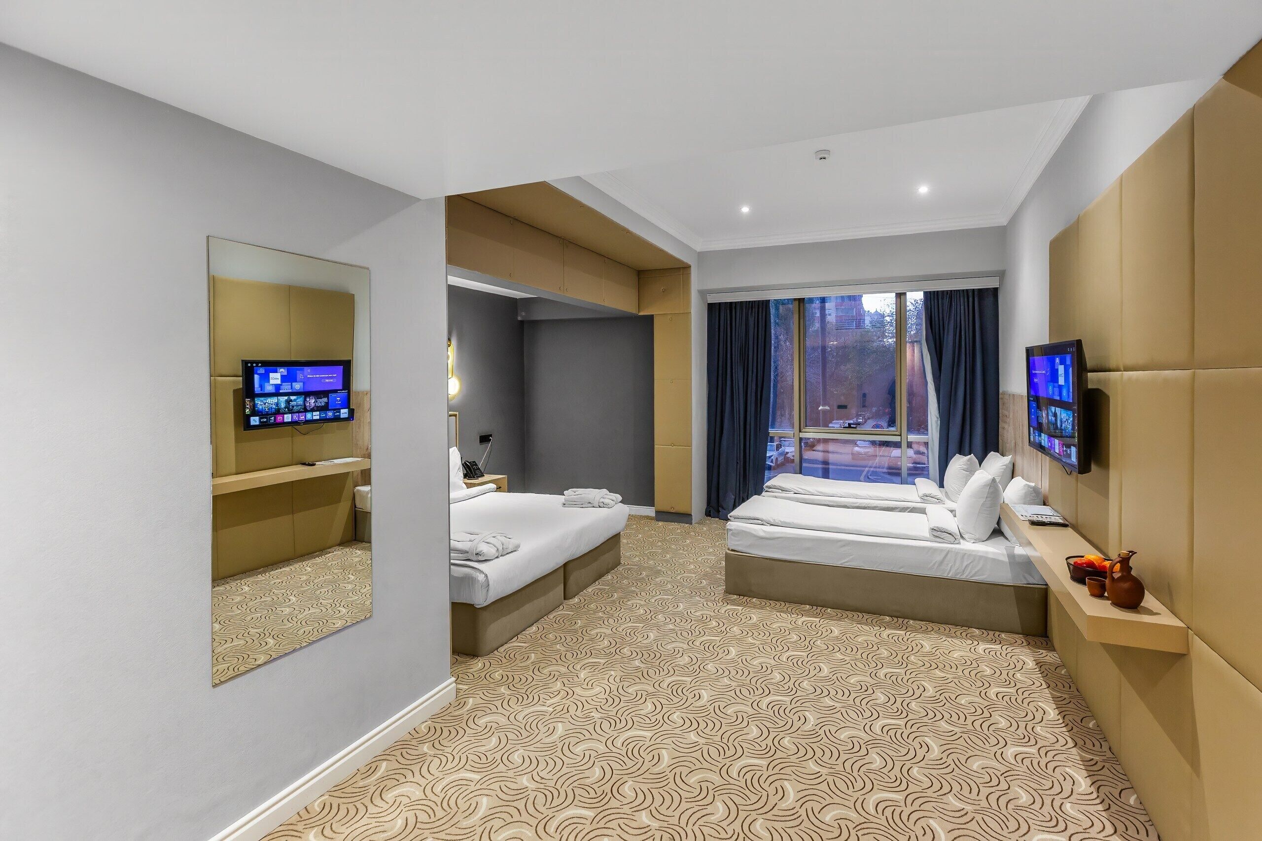 Quarto de hotel com duas camas, um espelho grande, televisão de tela plana e uma janela com cortinas.