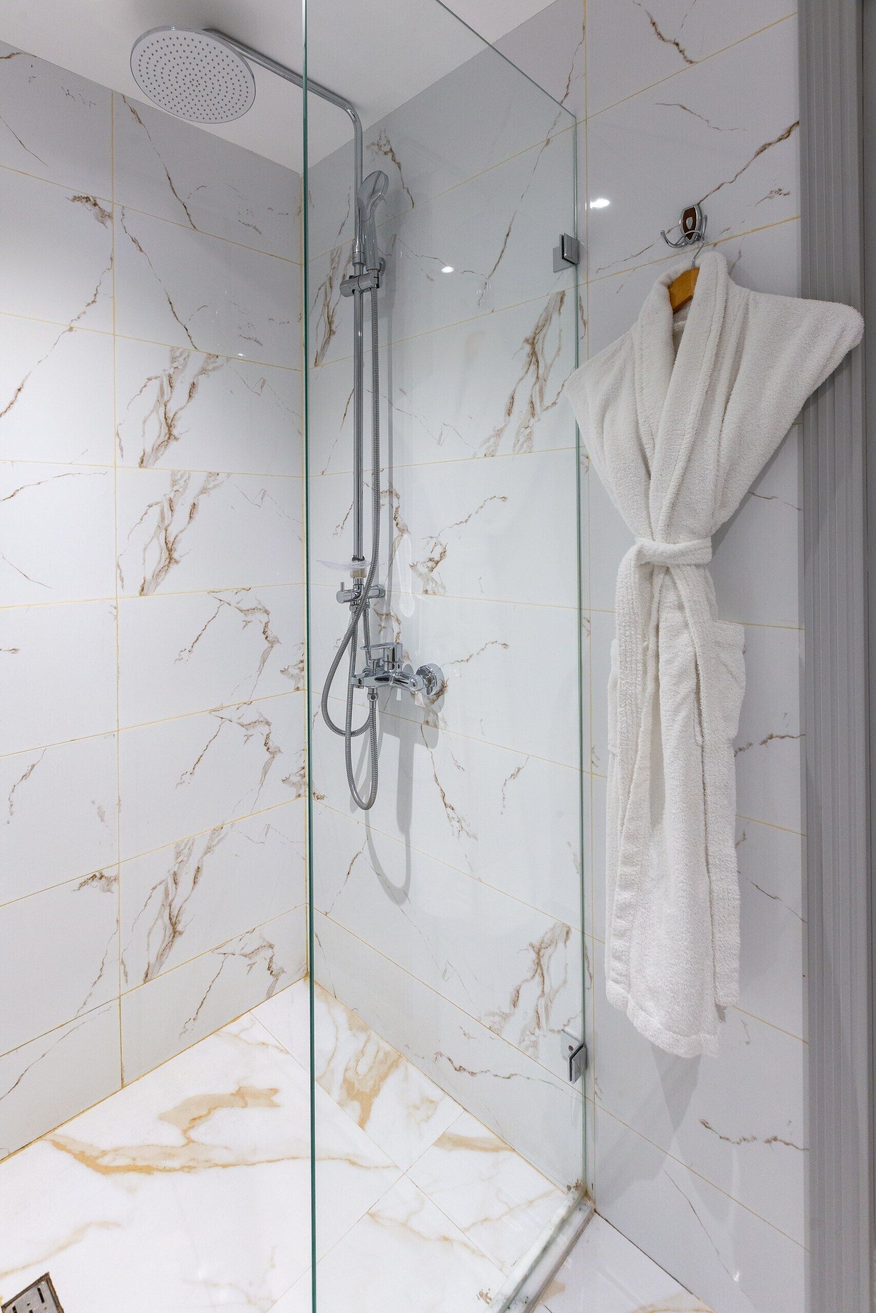 A glass-enclosed shower with a handheld showerhead and a handheld shower attachment.