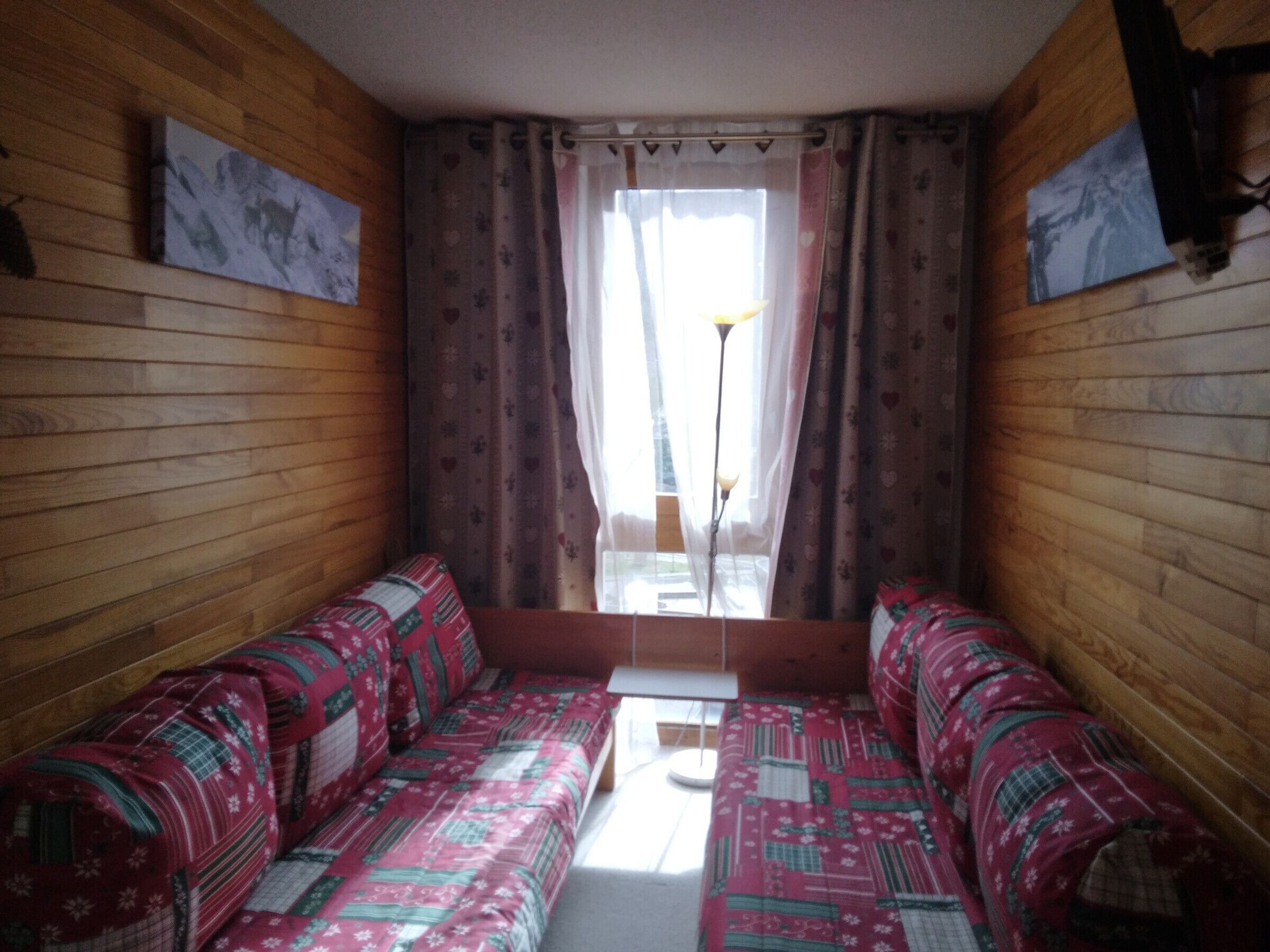 A cozy room with wooden walls, a patterned sofa, and a window with curtains.