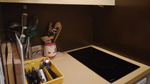 A kitchen with a black induction cooktop, wooden utensils, and a yellow utensil holder.