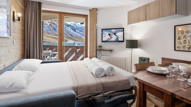 A hotel room with a bed, a dining table, a TV, and a view of mountains. - Val Thorens: Modern 4 ppl apartment with parking and piste view (Val Thorens)