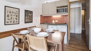 A compact kitchen with a microwave, dishwasher, and a dining area with a wooden table and chairs. - Val Thorens: Modern 4 ppl apartment with parking and piste view (Val Thorens)