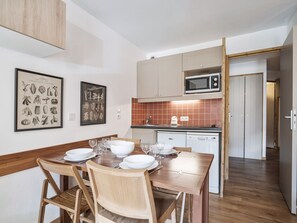 Una cucina compatta con forno a microonde, lavastoviglie e un'area pranzo con tavolo e sedie in legno.