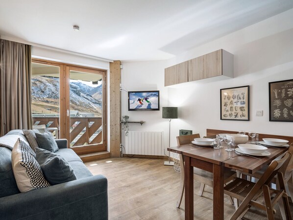 A modern living room with a sofa, a dining table set for four, and a large window with a view of mountains.