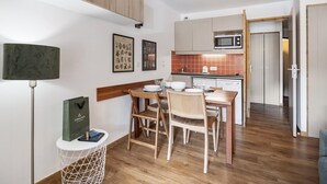 A compact kitchen with wooden cabinets, a microwave, and a dining area with a table and chairs. - Val Thorens: Modern 4 ppl apartment with parking and piste view (Val Thorens)
