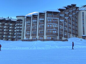 A multi-story hotel with balconies, snow-covered roofs, and a ski slope in the foreground.