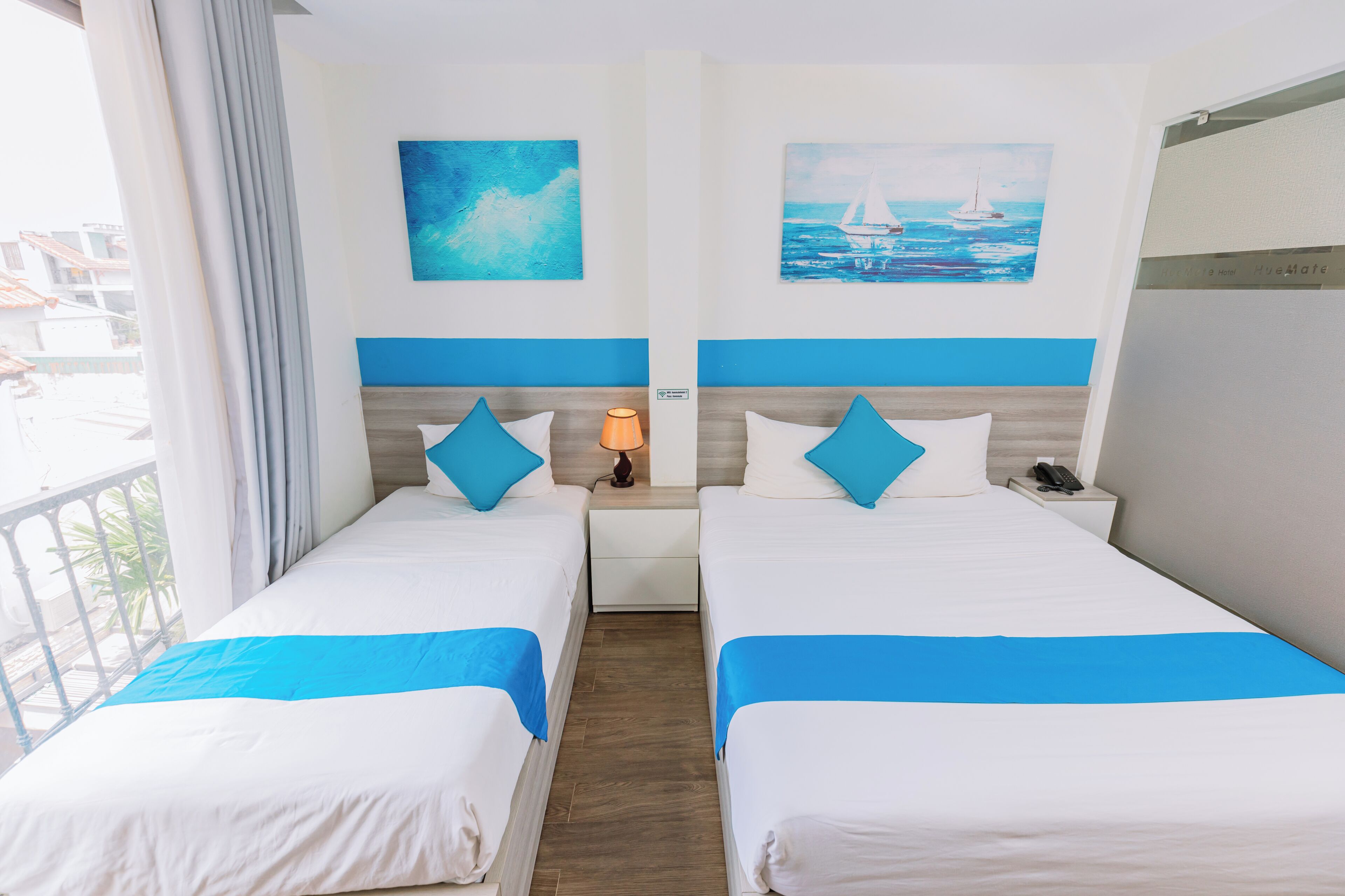 A hotel room with two beds, a nightstand with a lamp, and artwork on the walls.