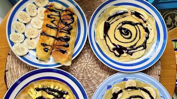 Four plates of food with bananas and chocolate sauce on a woven mat.