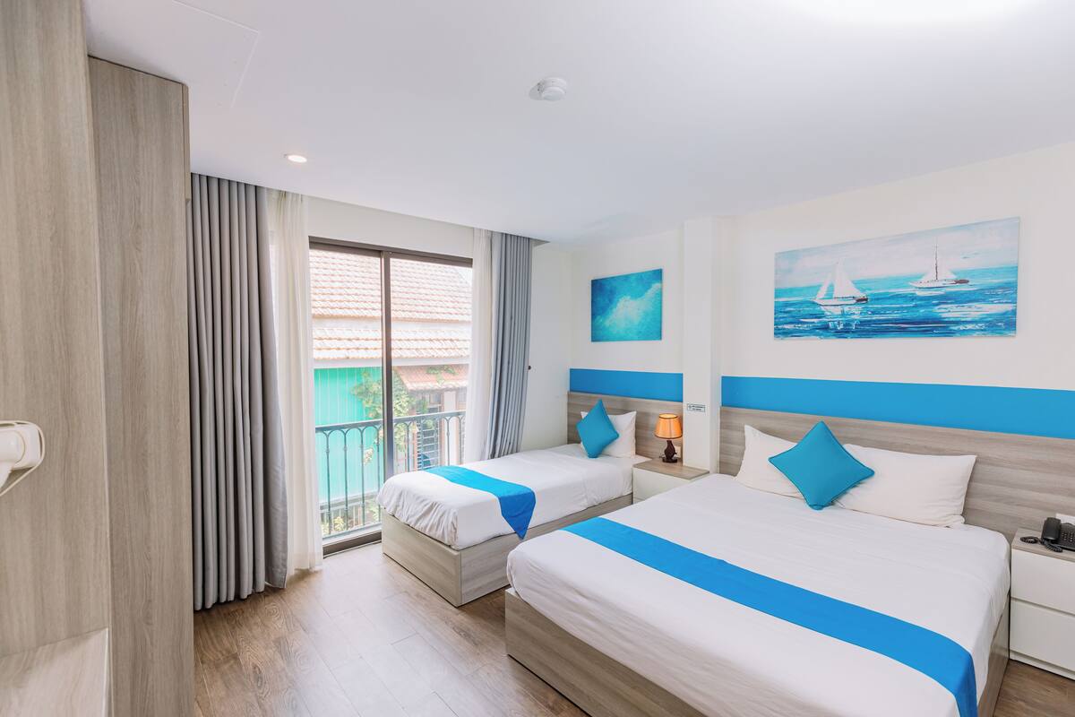 A hotel room with two beds, a balcony, and a painting of a sailboat.