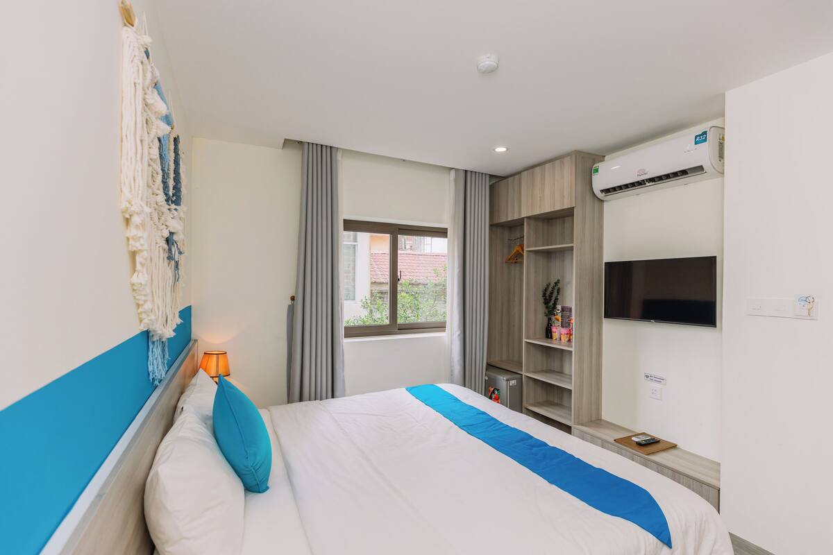 A hotel room with a bed, a nightstand, a lamp, a wardrobe, and an air conditioning unit.