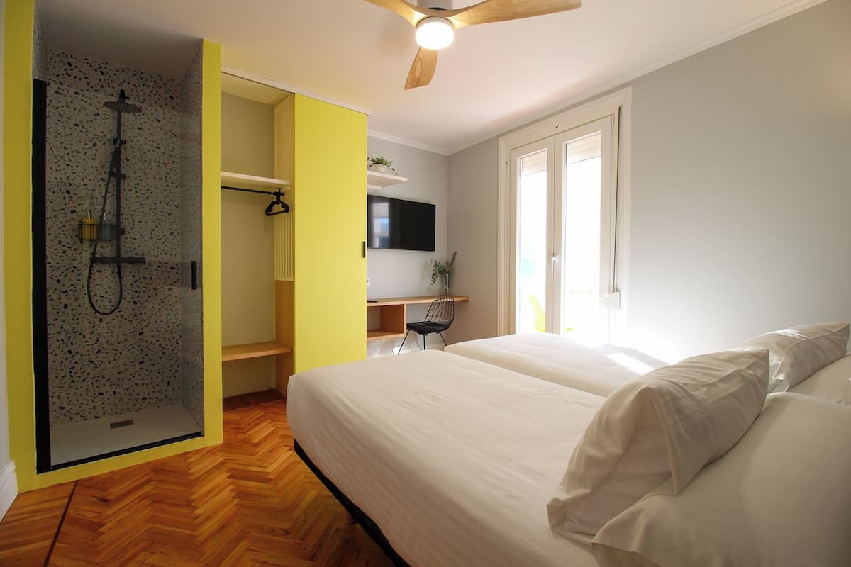 A bedroom with a bed, a shower area, a desk, and a TV.