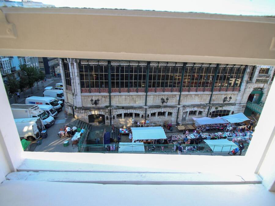 A view from a window overlooking a busy street with market stalls and parked vehicles.