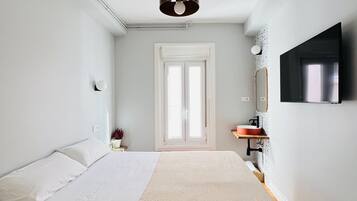 A bedroom with a bed, a bedside table, a mirror, a TV, and a window.