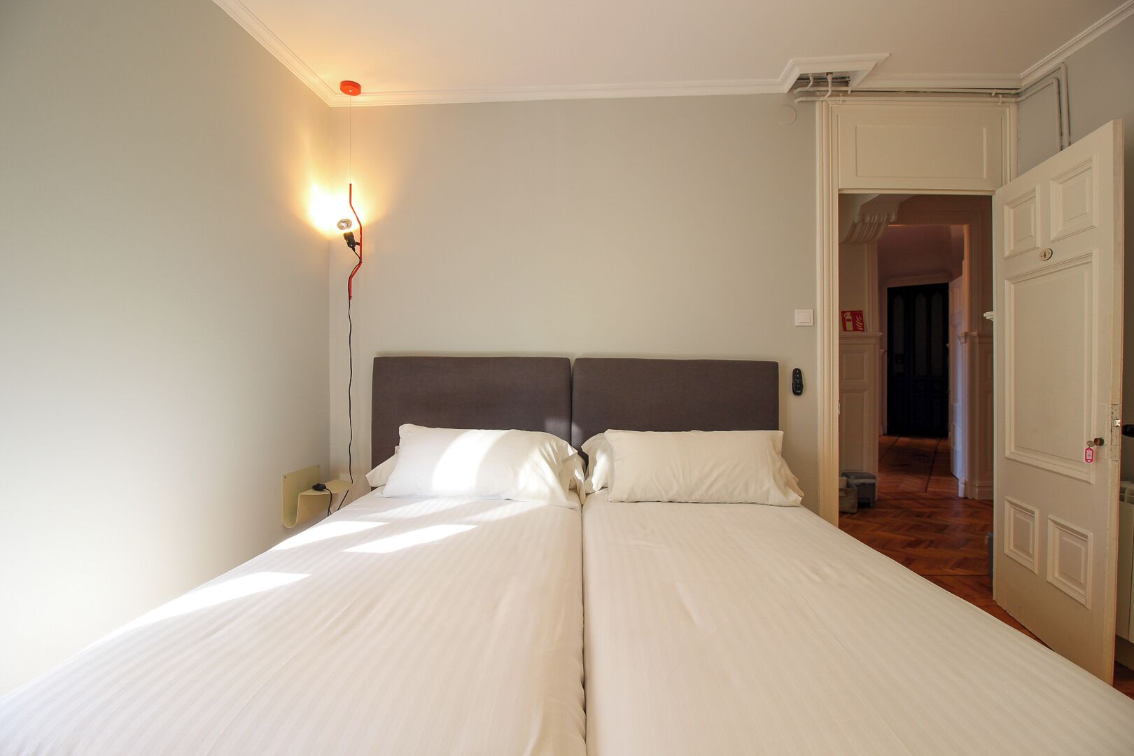 Una cama doble con ropa blanca en una habitación con piso de madera y puerta blanca.