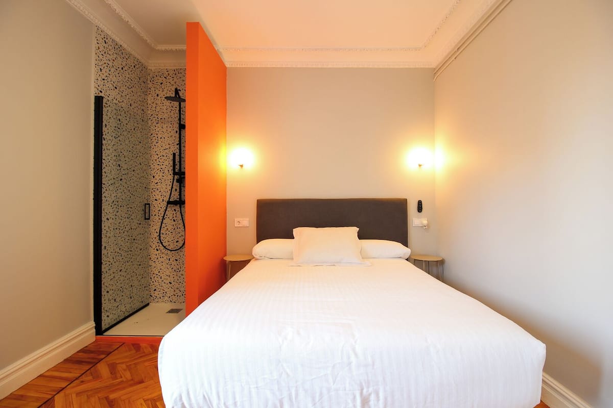 A hotel room with a large bed, two bedside lamps, a shower area, and a small table.