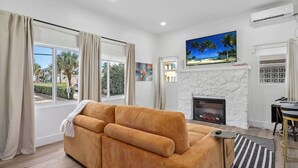 Una sala de estar con sofá, chimenea, televisor montado en la pared y vistas al exterior.