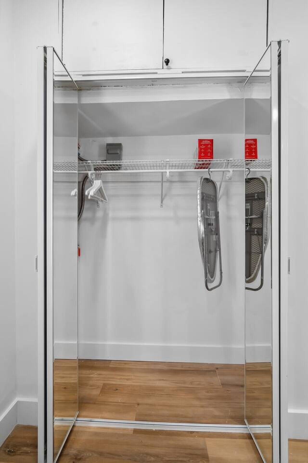 A walk-in closet with a mirrored door, a wooden floor, and a metal rack with hangers.