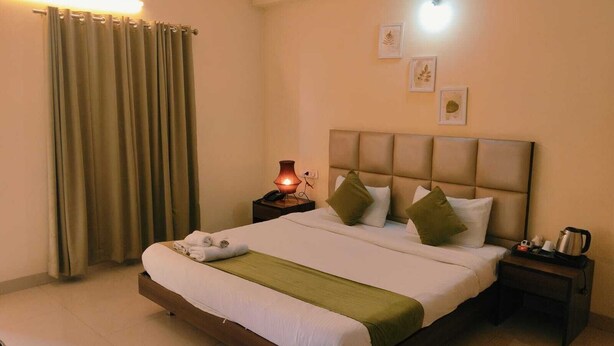 A neatly made bed with a green throw, a bedside lamp, and a nightstand with a kettle. - The Stem (Hyderabad)