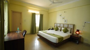 A hotel room with a bed, bedside table, desk, chair, curtains, and a ceiling fan. - The Stem (Hyderabad)