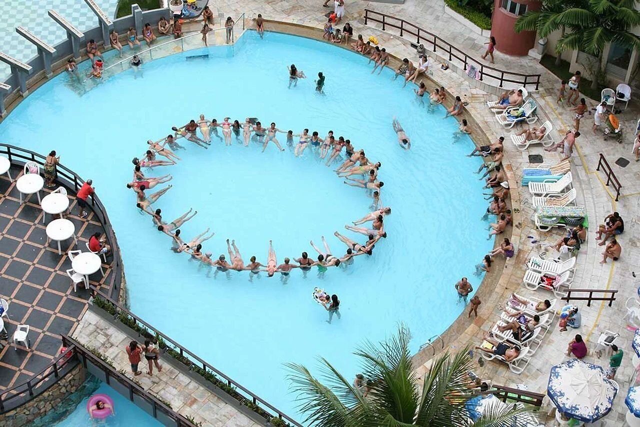 Uma grande piscina circular rodeada por espreguiçadeiras e guarda-sóis.